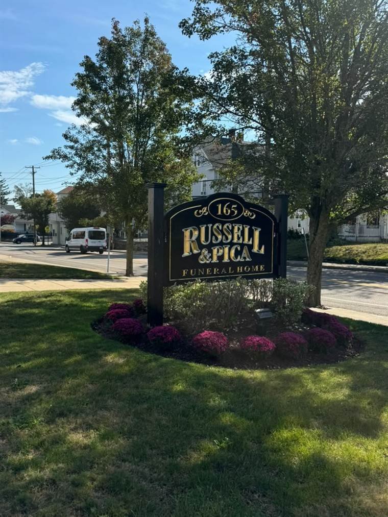Monument sign landscaped with seasonal mums and trimmed shrubs at Russell & Pica Funeral Home in Rockland, Massachusetts