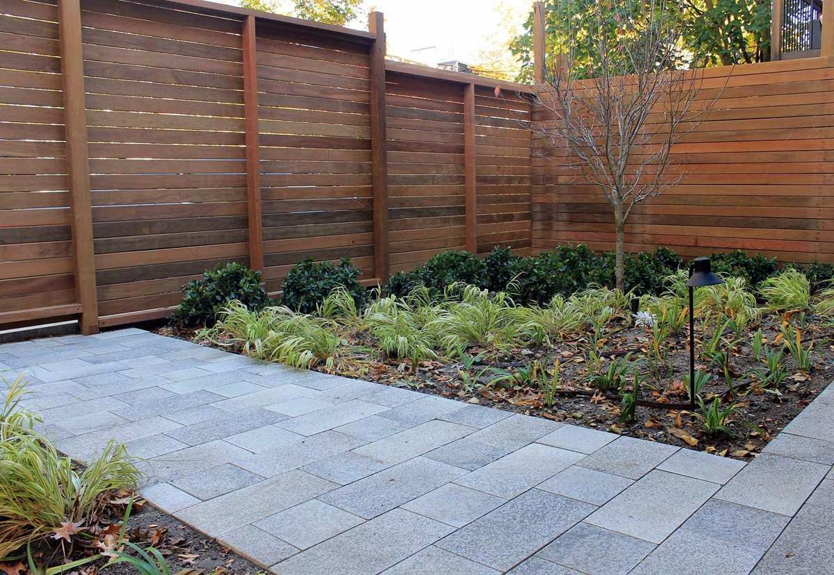 Horizontal wood fence bordering a gray paver patio with a planting bed of grasses and shrubs