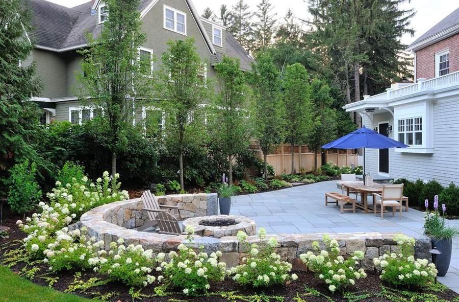 Curved stone seat wall and fire pit beside a bluestone patio with white hydrangeas